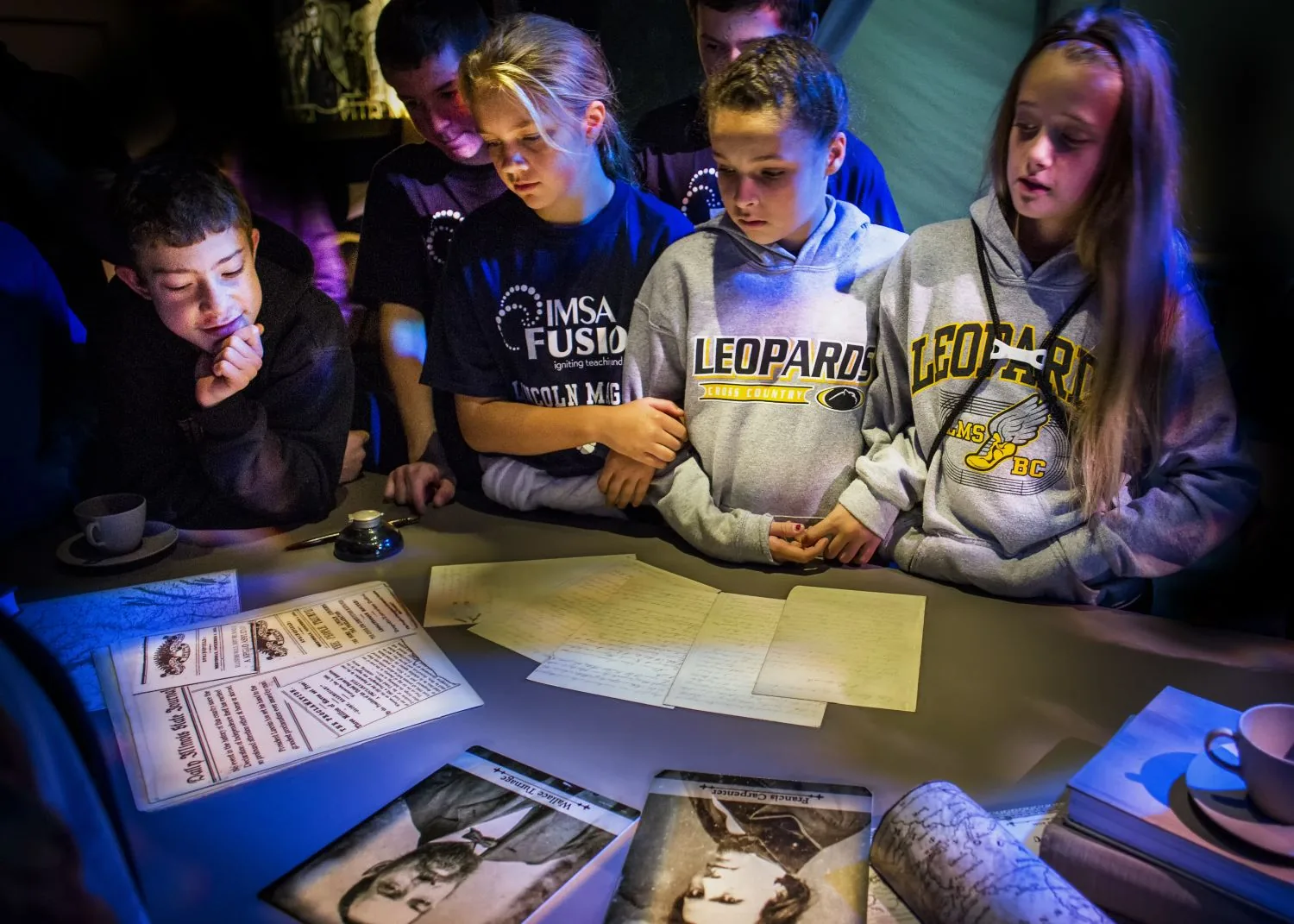 Students leaning over a lit table of reproduction artifacts.