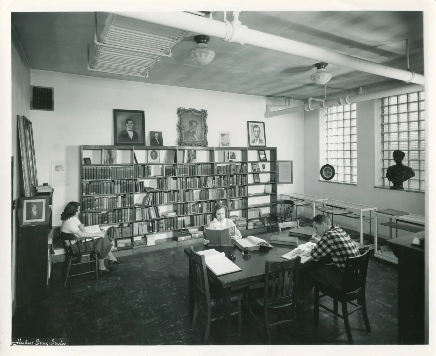 A black and white photograph of the Lincoln Room, a small study lined with framed portraits.